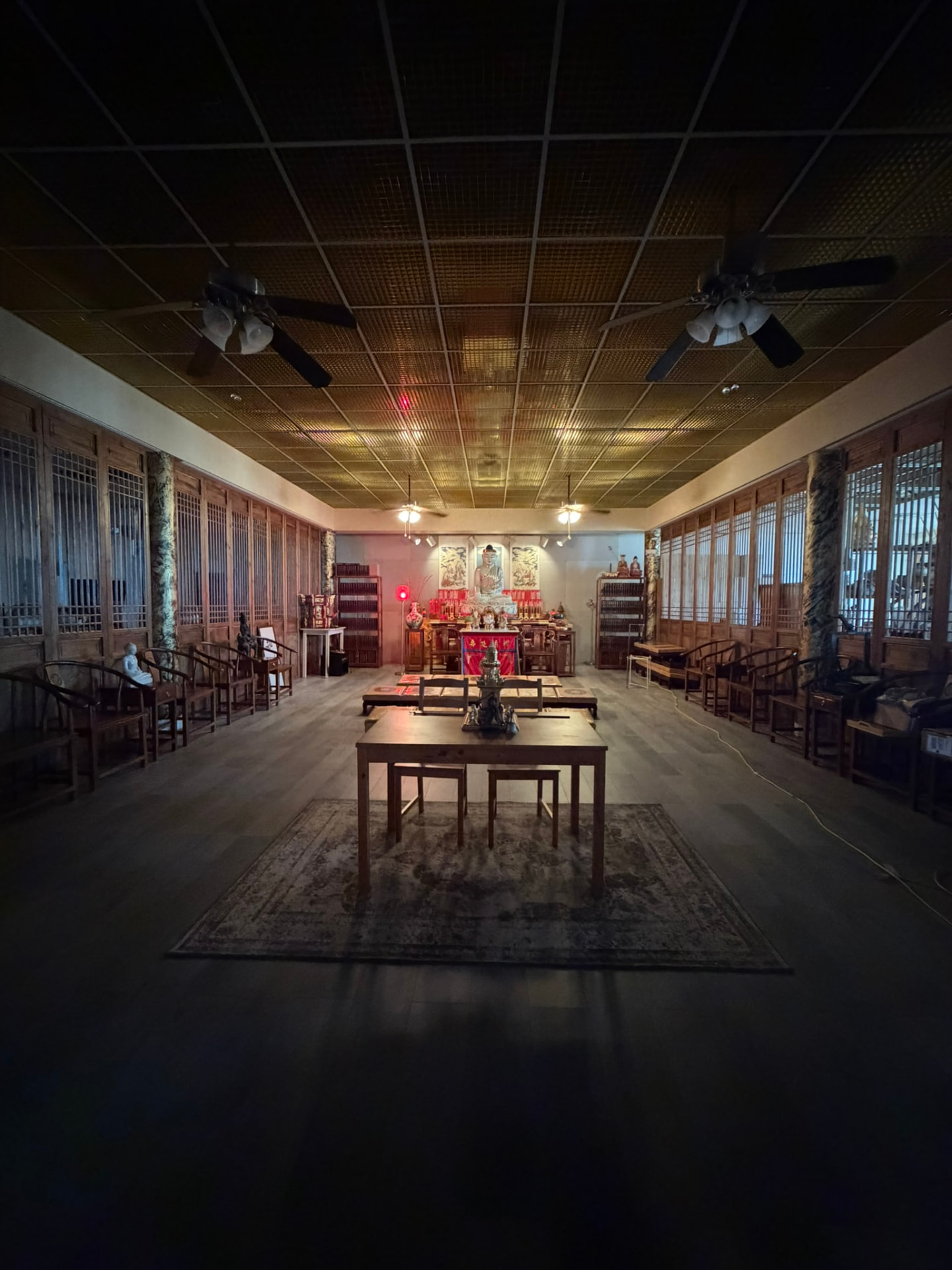 A quieter wood-panelled temple room with seating along both sides, central tables and an altar at the far end