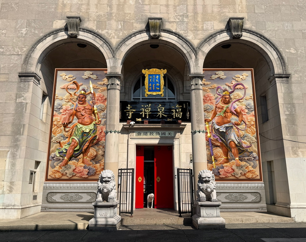 The full stone façade of the temple with three arches, guardian murals, red doors and stone lions